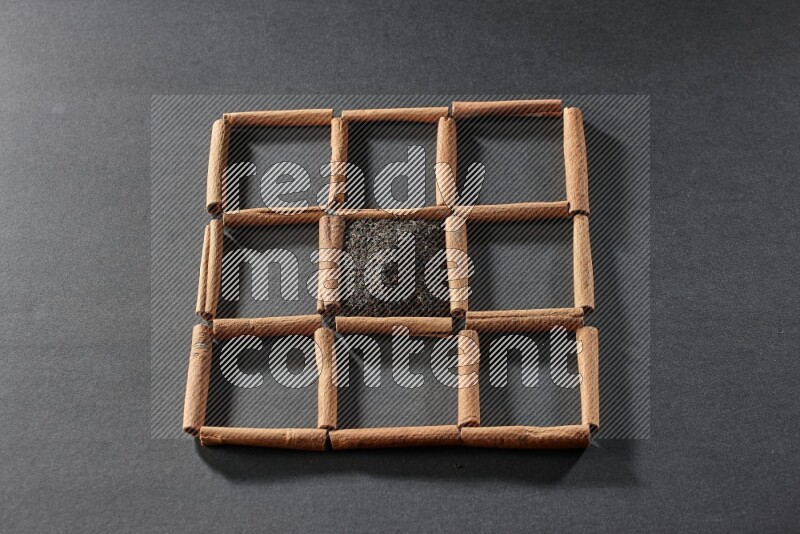 9 squares of cinnamon sticks full of tea in the middle surrounded by nutmeg, dried mint, cloves, dried basil, dried ginger, cinnamon, star anise and cardamom on black flooring