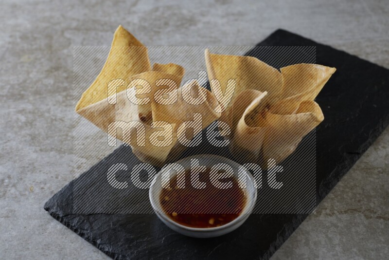 wonton cups with soy sauce ramkin on rectangle slate on grey textured counter top