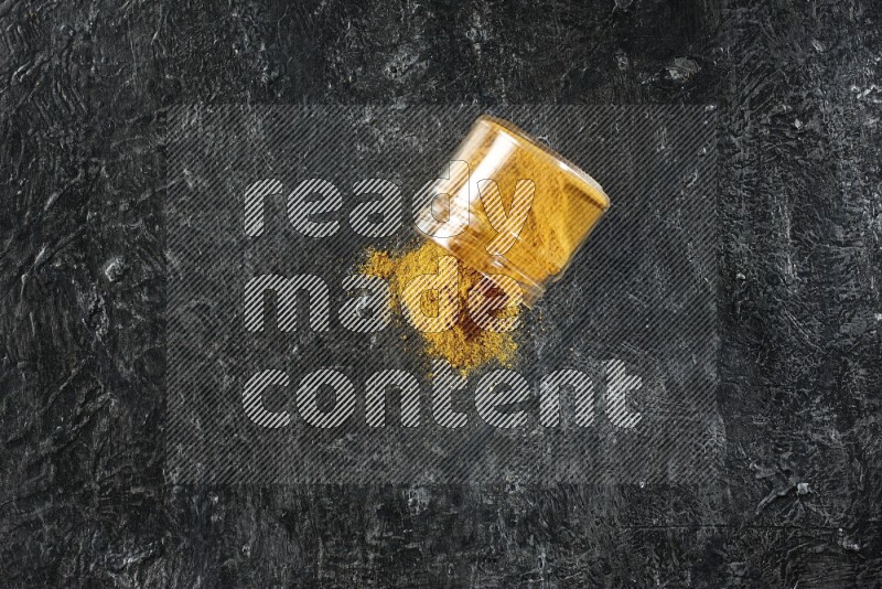 وعاء زجاجي مقلوب ممتلئ ببودرة الكركم والبودرة تناثرت منه على خلفية سوداء