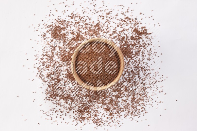 A wooden bowl full of garden cress seeds with more seeds spread on a white flooring