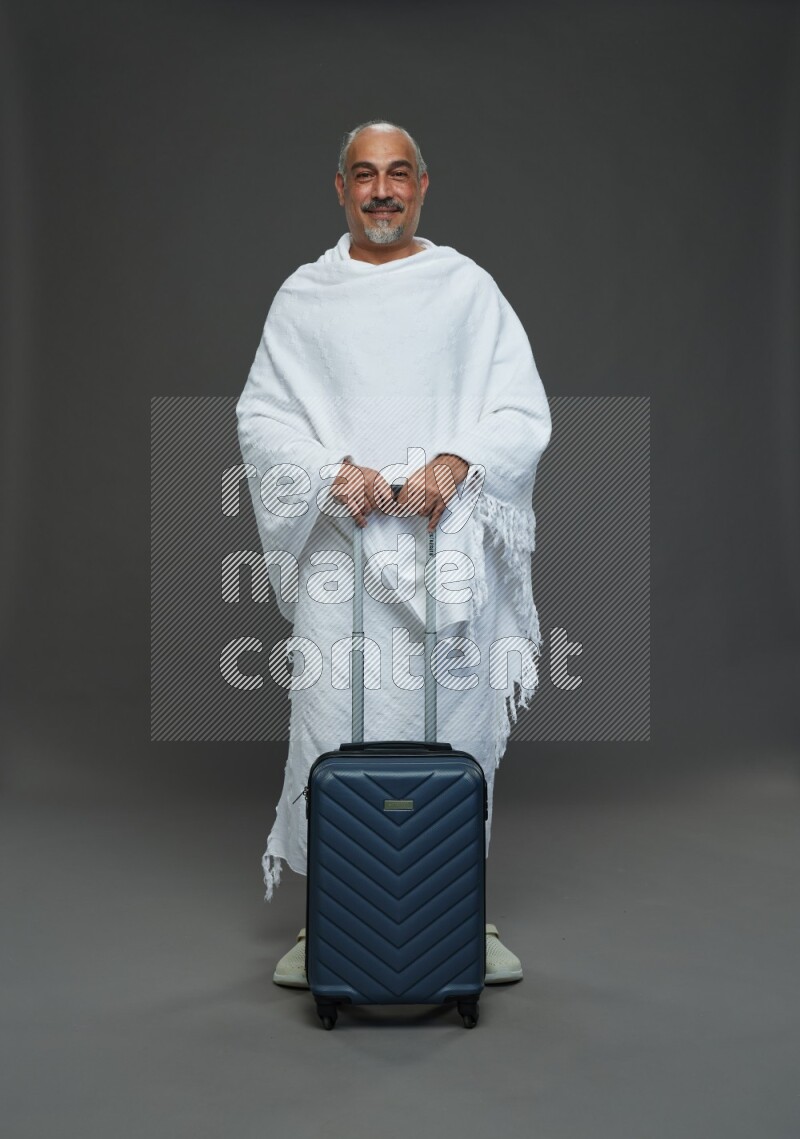 A man wearing Ehram Standing holding traveling bag on gray background