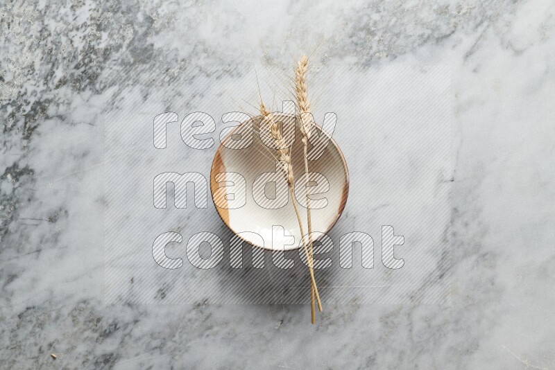 Wheat stalks on multicolored pottery plate on grey marble background