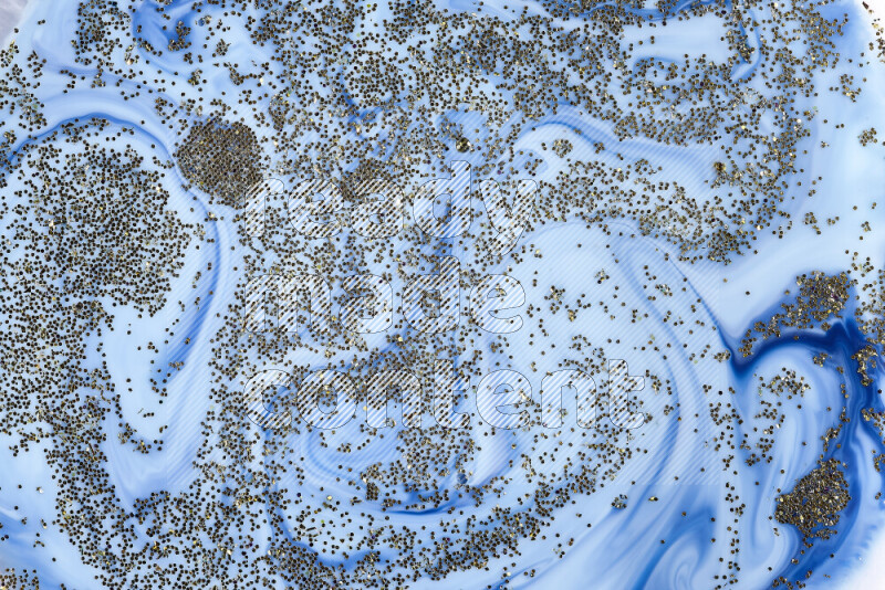 A close-up of sparkling gold glitter scattered on swirling blue background