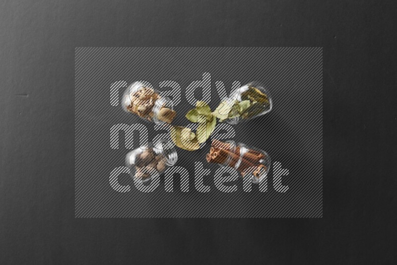 4 glass spice jars full of laurel bay leaves, ginger, cinnamon and nutmeg on black flooring