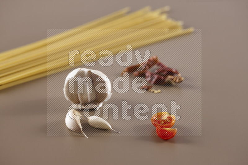 Raw pasta with different ingredients such as cherry tomatoes, garlic, onions, red chilis, black pepper, white pepper, bay laurel leaves, rosemary and cardamom on beige background