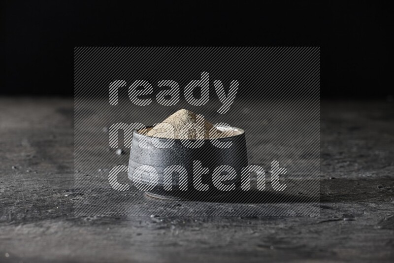 وعاء فخار أسود مملوء ببودرة الفلفل الأبيض على أرضية سوداء