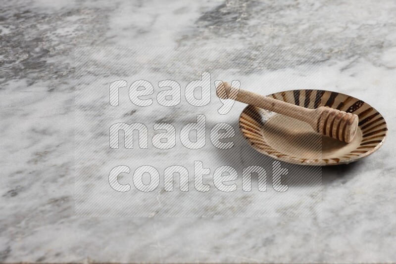 Multicolored pottery plate with wooden honey dipper in it on grey marble background