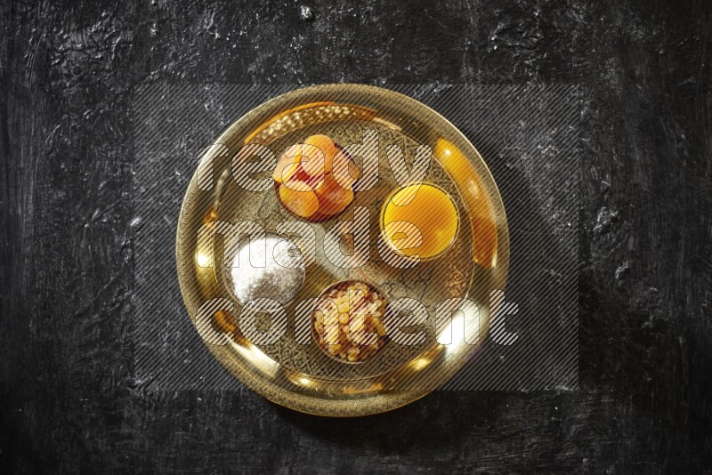 Dried fruits in metal bowls with qamar eldin on a tray in dark setup