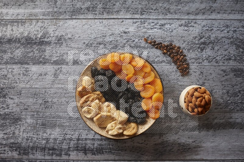 Dried fruits in a pottery plate with nuts and coffee in a dark setup