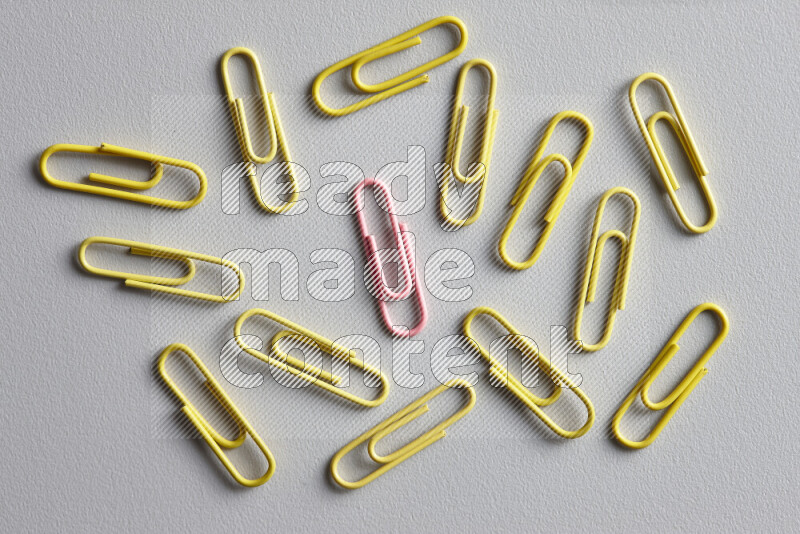 A bunch of yellow paper clips with a different colored paper clip in the center on grey background