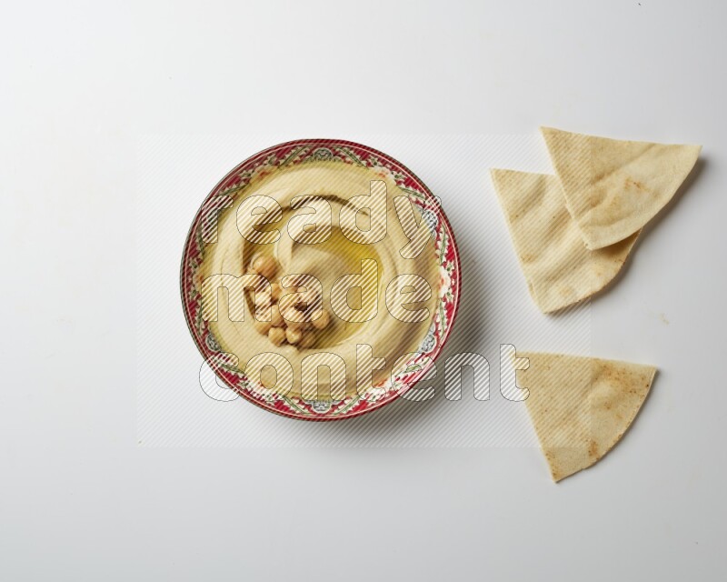 Hummus in a red plate with patterns garnished with roasted chickpeas  on a white background