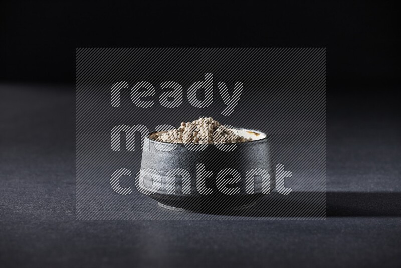 Black pottery bowl full of white pepper on black flooring