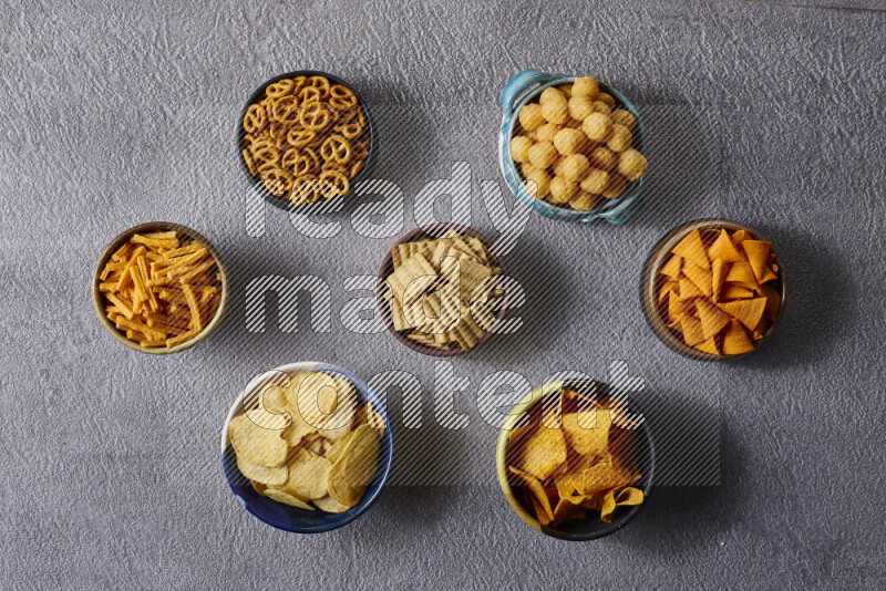 Assorted snacks in pottery bowls on grey background