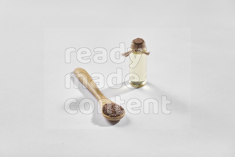 معلقة خشبية مليئة بحبوب بذر الكتان مع زجاجة من زيت بذر الكتان علي خلفية بيضاء