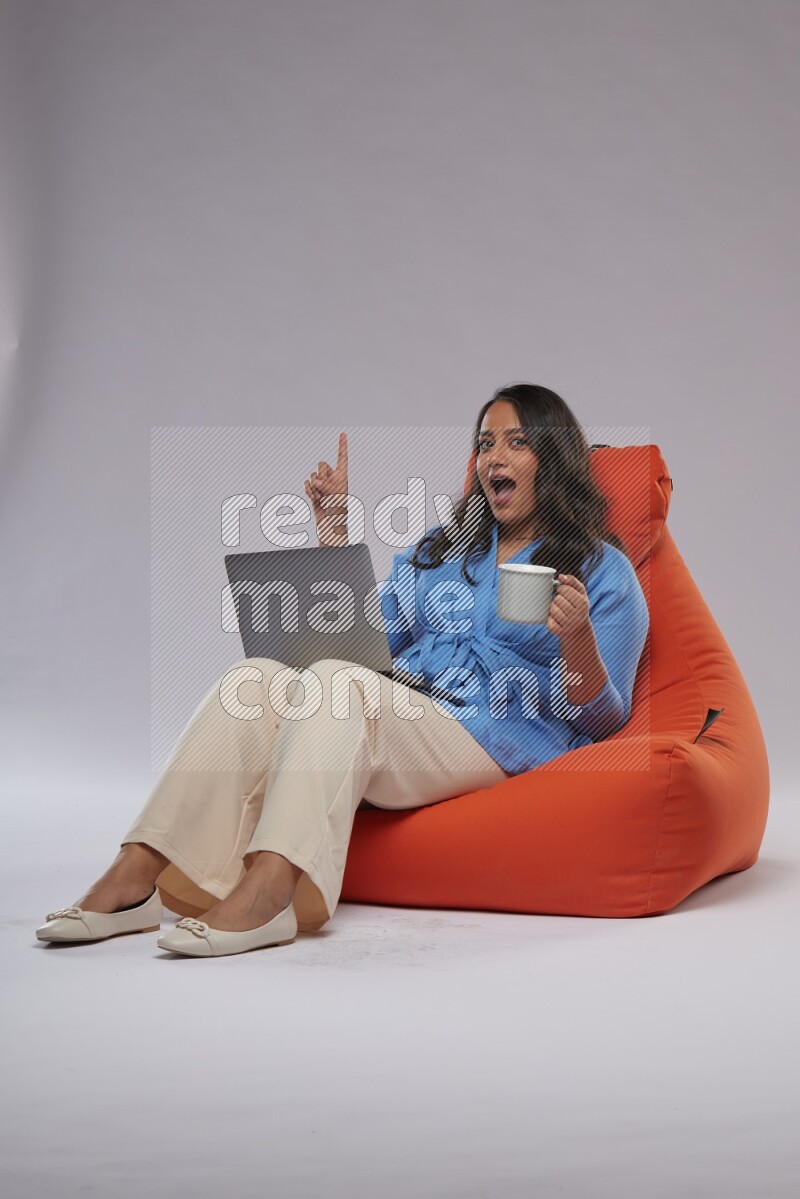 A woman sitting on an orange beanbag and working on laptop