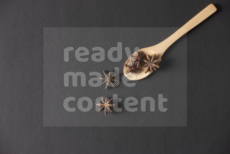 Star Anise in a wooden spoon on more stars anise filling the frame on black flooring