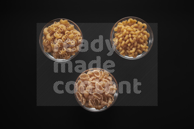 Different pasta types in glass bowls on black background