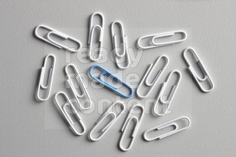 A bunch of white paper clips with a different colored paper clip in the center on grey background