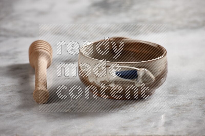 Multicolored pottery bowl with wooden honey dipper on the side on grey marble background