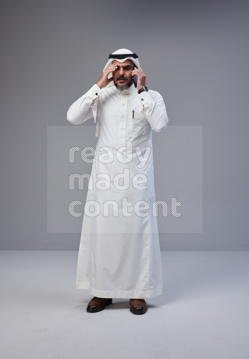 Saudi man Wearing Thob and white Shomag standing talking on phone on Gray background