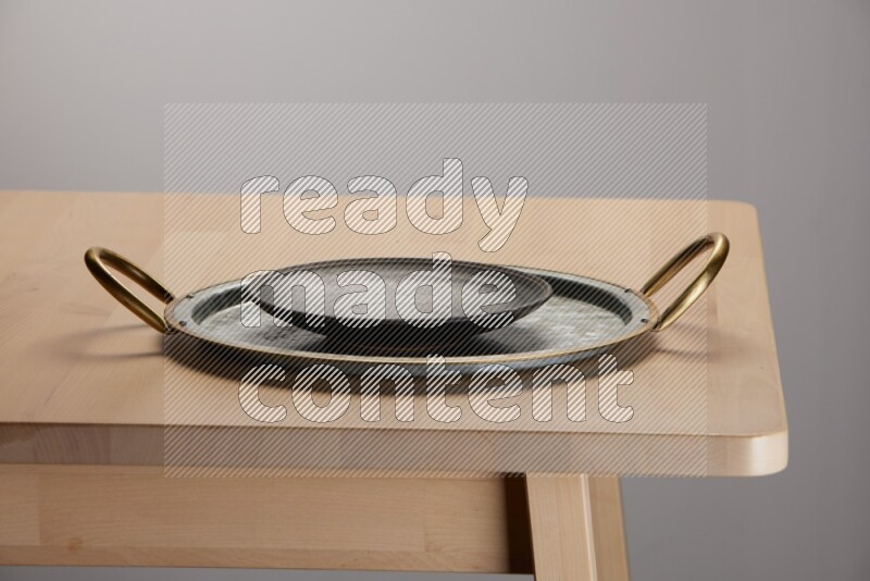 black plate placed on a rounded stainless steel metal tray with golden handels on the edge of wooden table