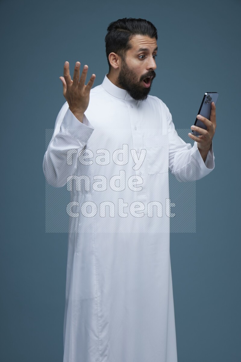 A man Texting in a blue background wearing Saudi Thob