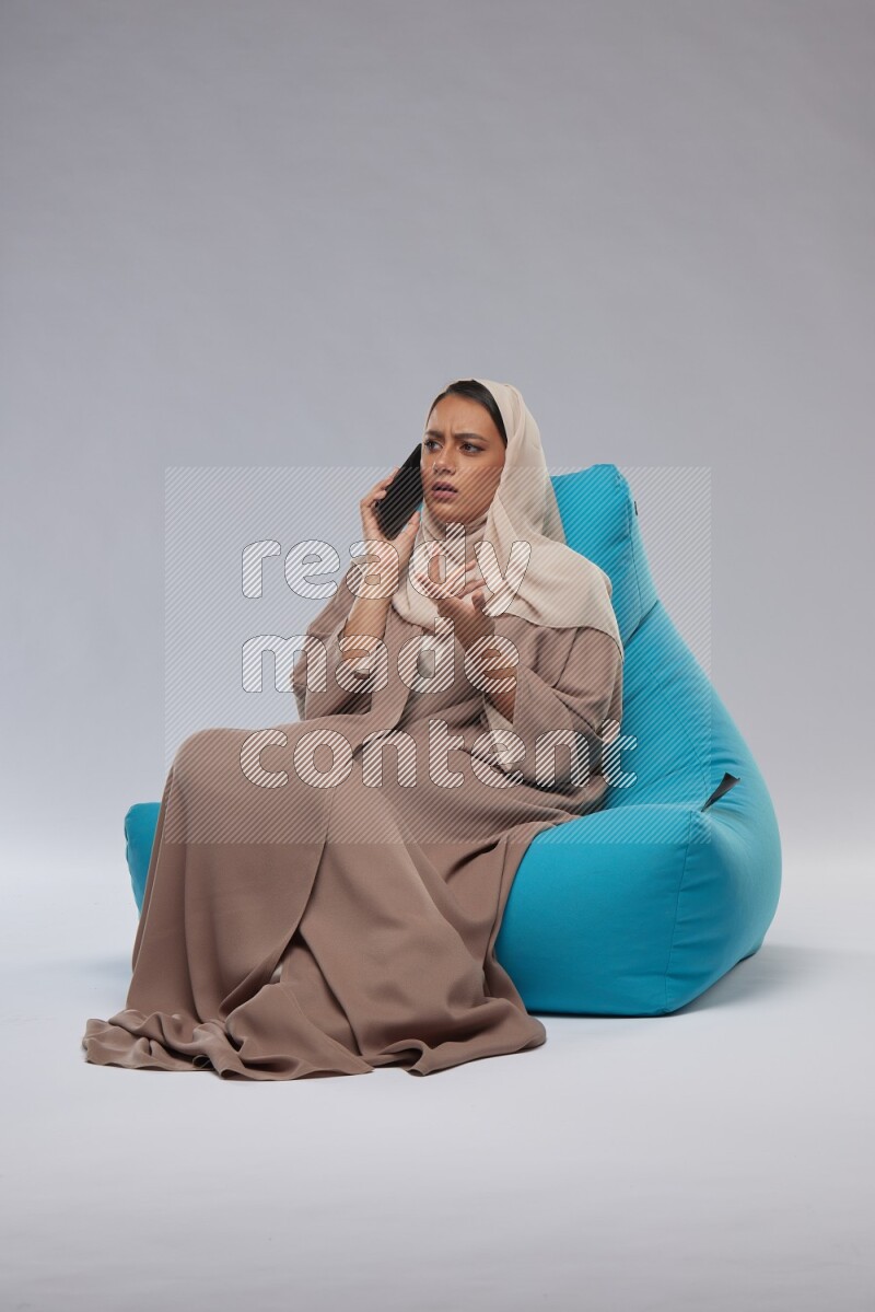 A Saudi woman sitting on a blue beanbag and working on laptop