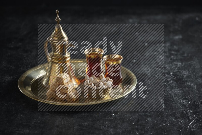 Oriental sweets with nuts and a drink on a metal tray in a dark setup