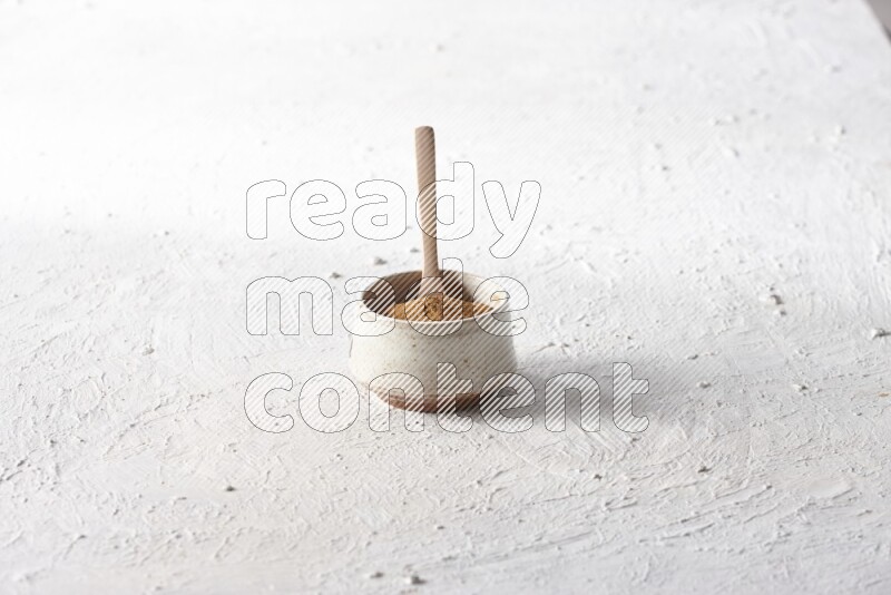 Ceramic beige bowl full of cinnamon powder with a wooden spoon on a textured white background