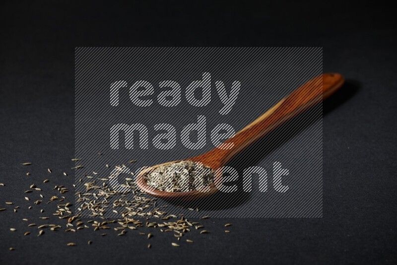 A wooden ladle full of cumin seeds on black flooring