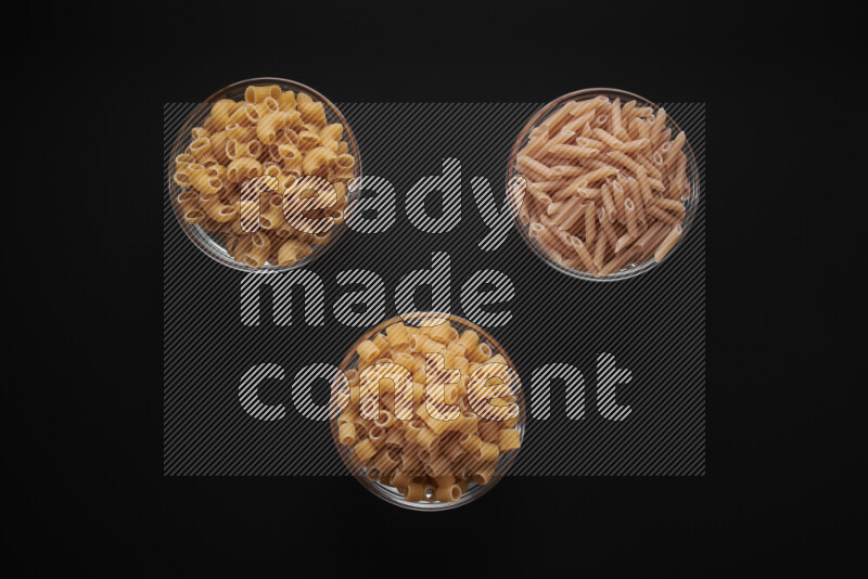 Different pasta types in glass bowls on black background