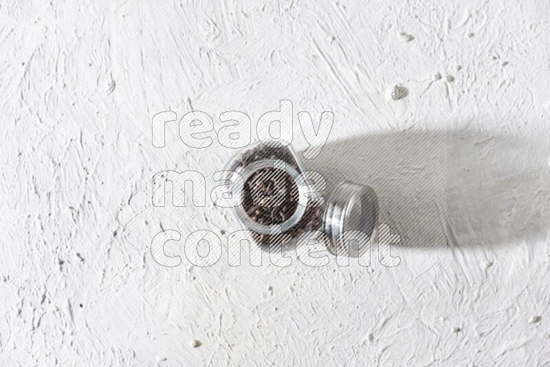 A glass spice jar full of cloves on textured white flooring