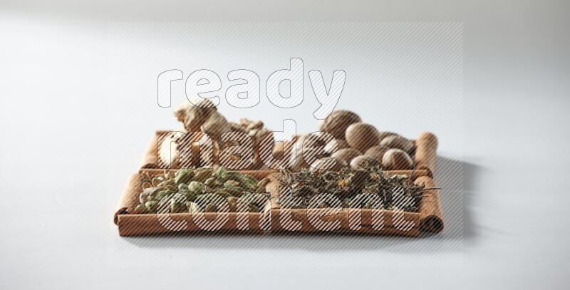 4 squares of cinnamon sticks full of nutmegs, dried ginger, cardamom and dried basil on white flooring