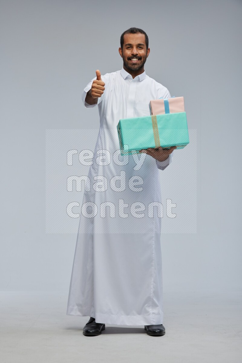 Saudi man Wearing thob standing holding gift box on Gray background