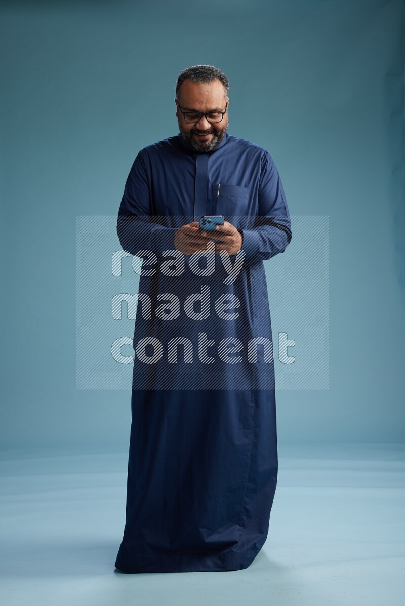 Saudi Man without shimag Standing texting on phone on blue background