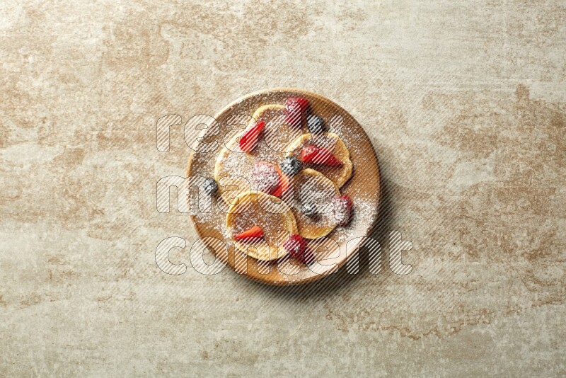 Five stacked mixed berries mini pancakes in a brown plate on beige background