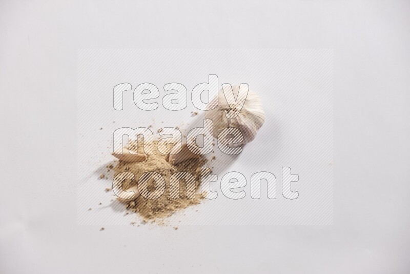 A small pile of garlic powder with some of cloves and a whole garlic bulb on a white flooring