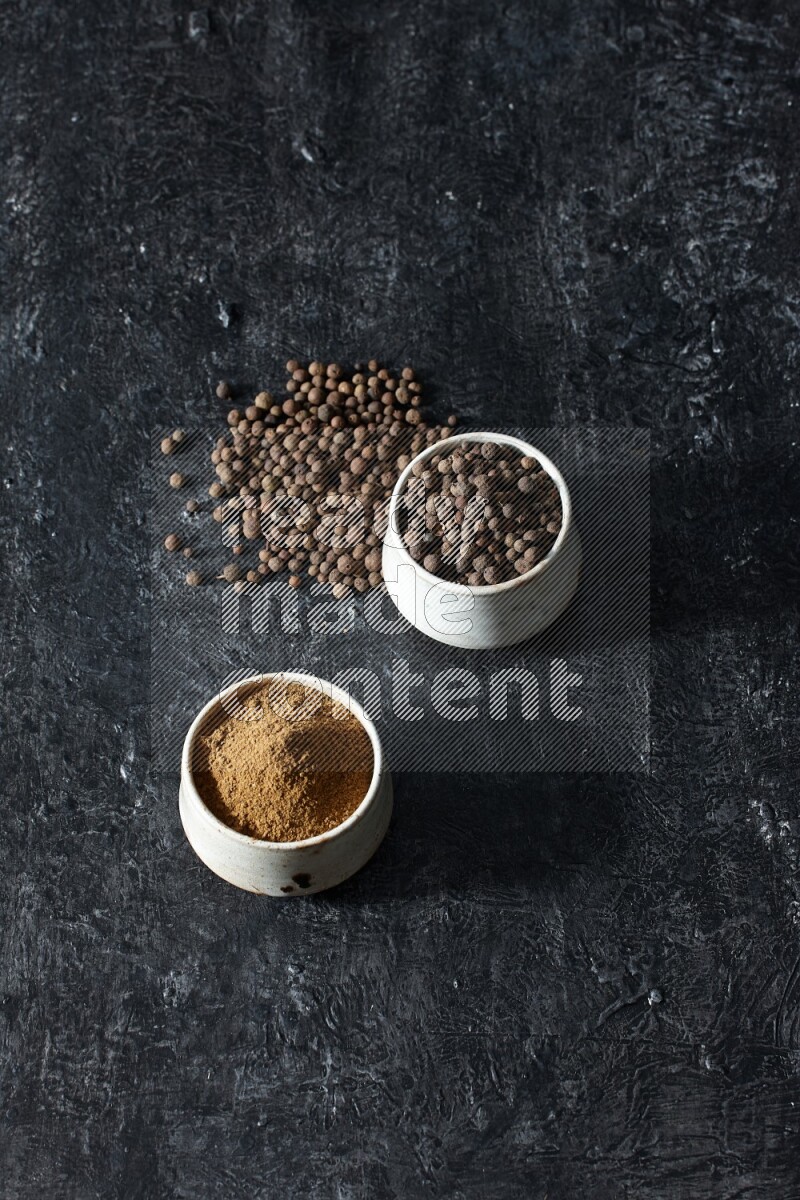 وعاءان بيج، أحدهما ممتلئ ببودرة بهار الفلفل الحلو والآخر بالحبوب وكلاهما متناثران على خلفية سوداء