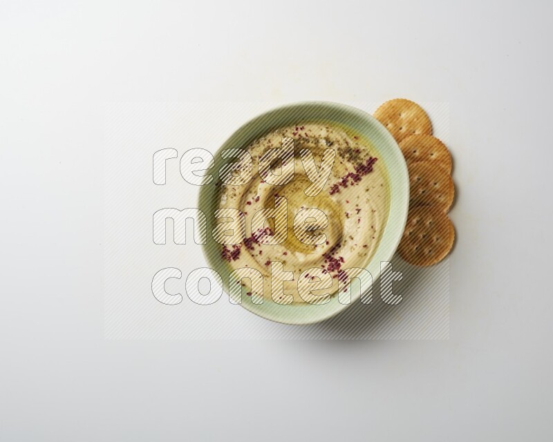 Hummus in a green plate garnished with zattar & sumak on a white background