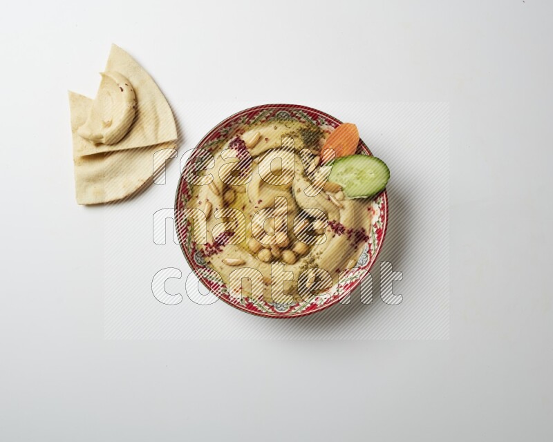Hummus in a red plate with patterns garnished with zaatar & sumak on a white background