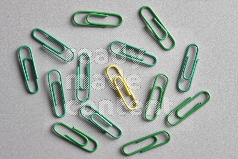 A bunch of green paper clips with a different colored paper clip in the center on grey background