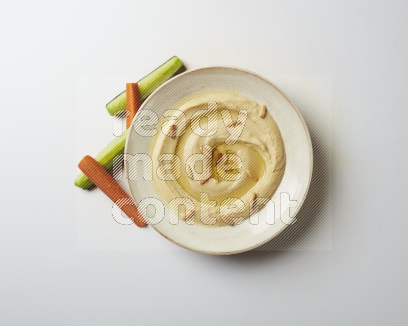 Hummus in a pottry plate garnished with pine nuts on a white background