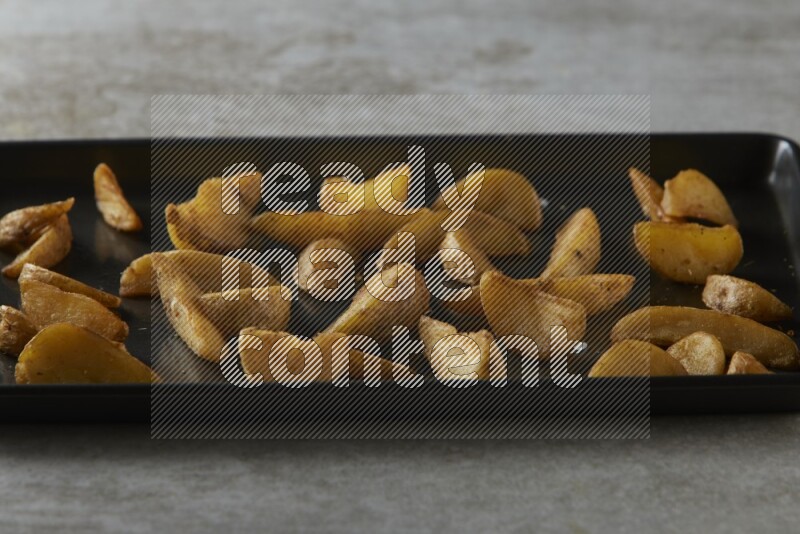 wedges potato in a black stainless steel rectangle tray on grey textured counter top