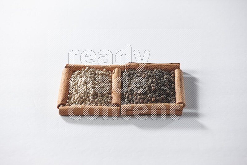 2 squares of cinnamon sticks full of black pepper and white pepper on white flooring