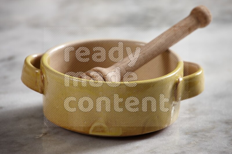 Multicolored pottery bowl with wooden honey dipper in it on grey marble background
