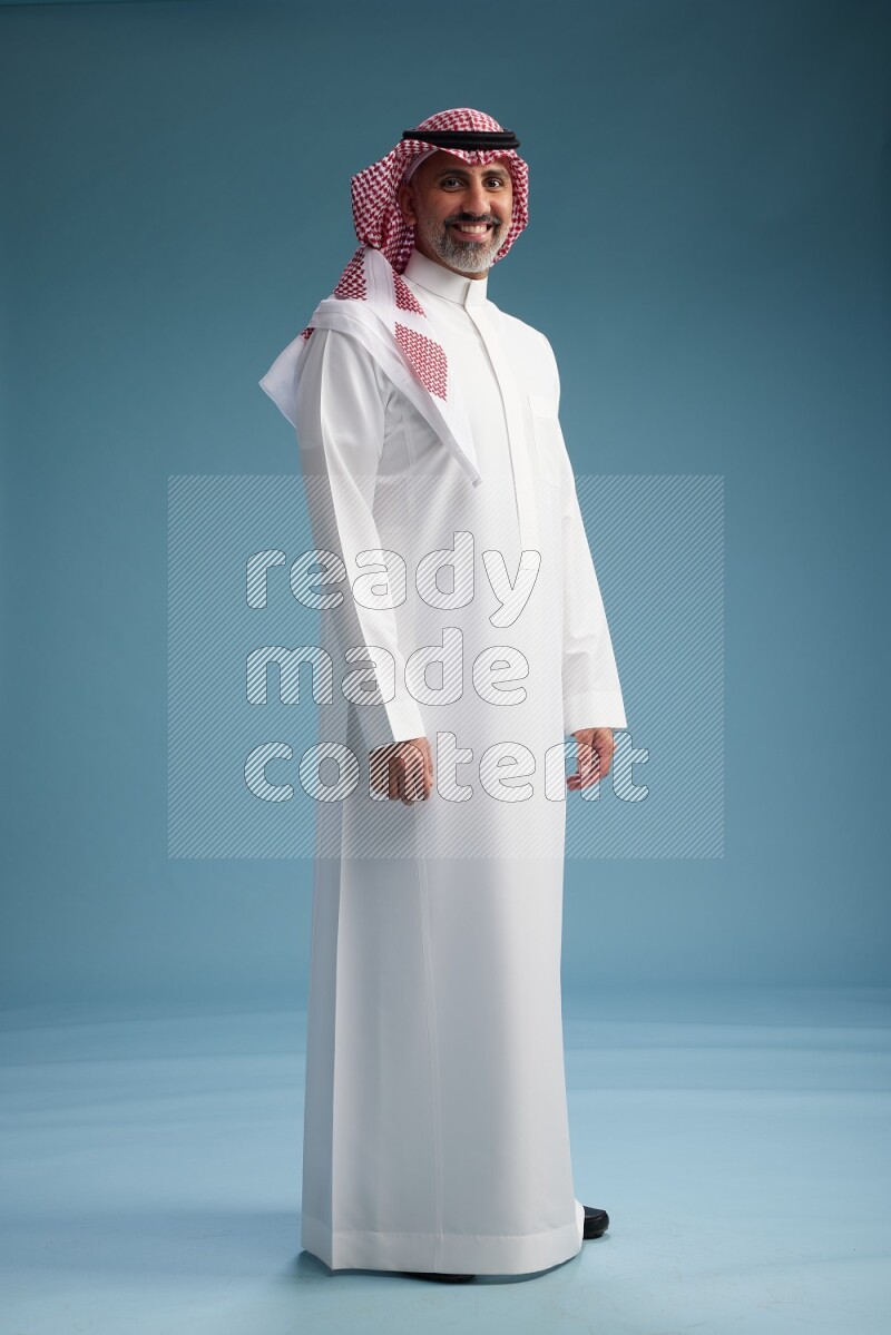 Saudi man wearing thob and shomagh posing to the camera on blue background