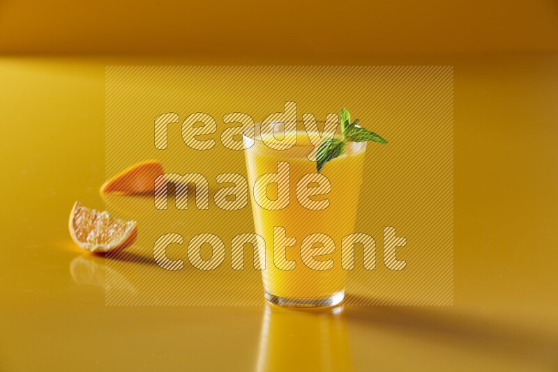 glass of orange juice with  mint on yellow background