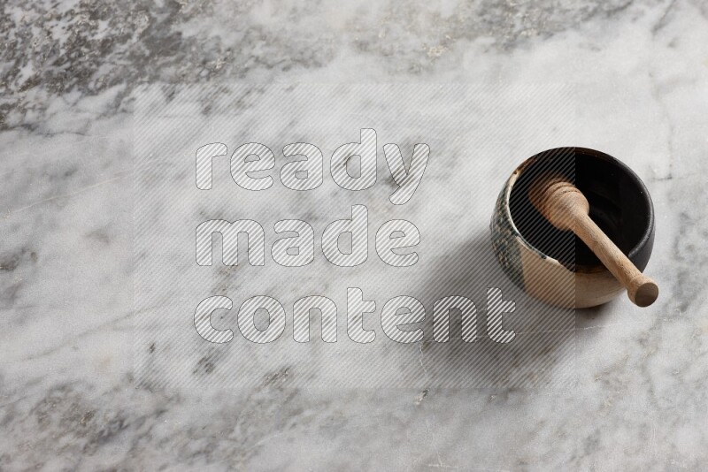 Multicolored pottery bowl with wooden honey dipper in it on grey marble background
