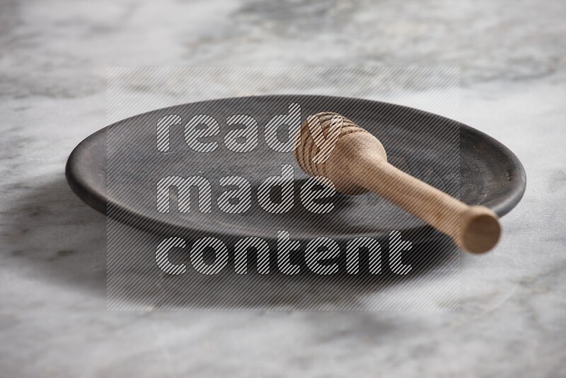 Black pottery plate with wooden honey dipper in it on grey marble background