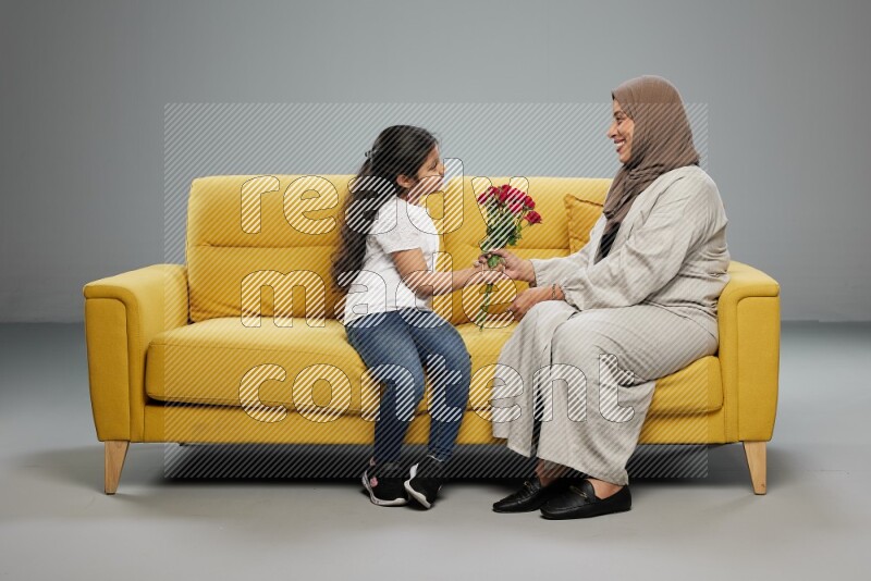 A girl sitting giving flowers to her mother on gray background